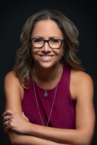 Professor Clare Wright - Photographic Portrait - Black background. Woman wearing glasses, and a burgundy coloured top.